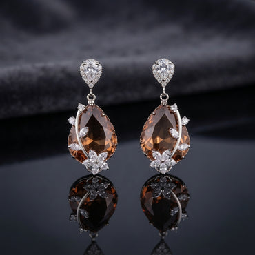 CZ Pear Halo Stud and Large Teardrop Floral Marquise Drop Earrings Sapphire Blue colorway flat lay on dark mirror surface with dark satin backdrop showing rhodium silver-tone pair with pear white CZ halo stud top and large faceted deep London blue teal teardrop CZ pendant with marquise white CZ floral crown and leaf accents with sharp mirror reflection below