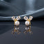 CZ Pear Leaf Branch Pearl Stud Earrings in Gold pair on dark slate mirror surface with grey silk backdrop showing 18K gold-tone slim Y-shaped branch stud with large pear-cut CZ and smaller round CZ as leaves cradling a lustrous round white pearl at the fork with mirror reflection below
