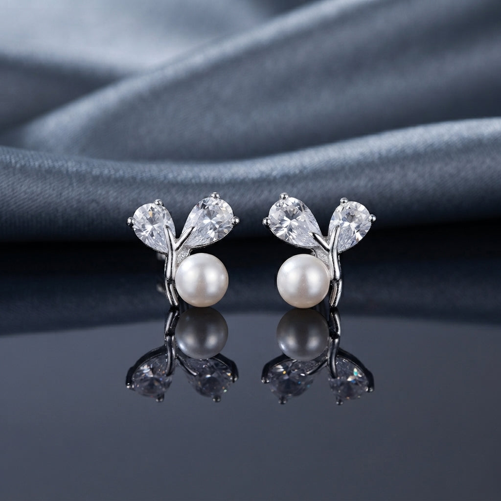 CZ Pear Leaf Branch Pearl Stud Earrings in Silver pair on dark slate mirror surface with grey silk backdrop showing rhodium-plated slim Y-shaped branch stud with large pear-cut CZ and smaller round CZ as leaves cradling a lustrous round white pearl at the fork with mirror reflection below