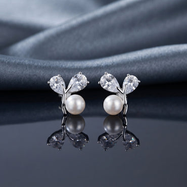 CZ Pear Leaf Branch Pearl Stud Earrings in Silver pair on dark slate mirror surface with grey silk backdrop showing rhodium-plated slim Y-shaped branch stud with large pear-cut CZ and smaller round CZ as leaves cradling a lustrous round white pearl at the fork with mirror reflection below