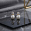 CZ Solitaire Pearl Drop Stud Earrings in Gold pair on black hexagonal tray with grey marble backdrop showing 18K gold-tone round brilliant CZ solitaire in 4-prong setting above large lustrous round white pearl with mirror reflection below