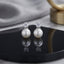 CZ Solitaire Pearl Drop Stud Earrings in Silver pair on black hexagonal tray with marble and gold prop backdrop showing rhodium-plated round brilliant CZ solitaire in 4-prong setting above large lustrous round white pearl with mirror reflection below