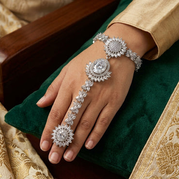 CZ Sunflower Cluster Hath Phool Hand Bracelet Ring Gold lifestyle shot worn on model hand over green velvet cushion with gold brocade fabric showing champagne CZ sunflower clusters on wrist and connected finger ring in 18K gold-tone plating