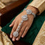 CZ Sunflower Cluster Hath Phool Hand Bracelet Ring Gold lifestyle shot worn on model hand over green velvet cushion with gold brocade fabric showing champagne CZ sunflower clusters on wrist and connected finger ring in 18K gold-tone plating