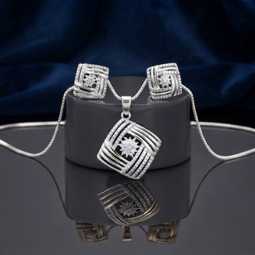 CZ Woven Basket Weave Square Pendant Necklace and Stud Earrings Set in gold-tone flat lay on grey mirror surface with navy blue velvet backdrop showing 2-piece set with tilted square woven basket weave pendant with white CZ micro-pavé border and CZ starburst center and matching square stud earrings with mirror reflection