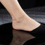 Dainty Gold Chain Anklet in 18K gold-tone worn on bare ankle with black pointed heel in editorial model shot showing ultra-slim minimalist fine box chain delicately wrapped around ankle with mirror reflection below on black lacquer surface