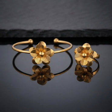 Gold 3D Five-Petal Ribbed Stripe Flower Open Cuff Bangle and Ring Matching Jewelry Set on dark grey glossy surface with charcoal stone backdrop showing 22K warm matte yellow gold-tone open cuff wire bangle lying flat with matching open adjustable ring standing beside it both featuring 3D five-petal rounded flowers with parallel horizontal ribbed stripe engraved petals and raised polished dome centres with sharp mirror reflections below