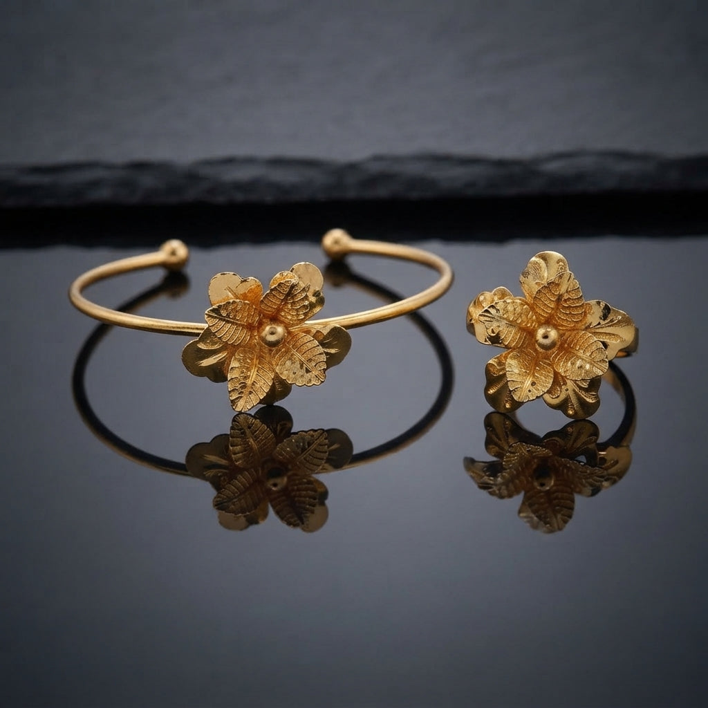Gold 3D Four-Petal Clover Flower Filigree Open Cuff Bangle and Ring Matching Jewelry Set on dark grey slate surface with charcoal stone backdrop showing 22K warm yellow gold-tone open cuff wire bangle lying flat with matching open adjustable ring standing beside it both featuring 3D four-petal clover hydrangea flowers with dense botanical filigree repoussé textured petals scalloped edges and raised polished dome centres with mirror reflections below