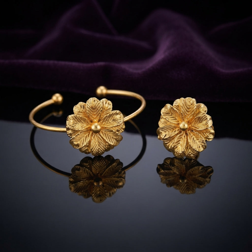 Gold 3D Sculptural Peony Flower Open Cuff Bangle Bracelet Set of 2 pair standing side by side on dark grey mirror surface with deep purple amethyst velvet backdrop showing 22K warm matte yellow gold-tone open cuff wire bangles each with large 3D sculptural multi-layered peony dahlia flower featuring herringbone feather-vein textured petals and raised polished dome centre with sharp mirror reflections below