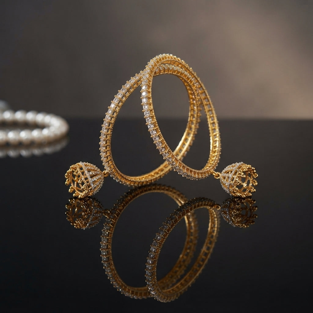 Gold AD CZ Micro-Pavé Slim Bangle Pair with Filigree Ball Charm leaning upright on dark black mirror surface with taupe backdrop and pearl necklace beside showing two fully AD CZ micro-pavé encrusted slim gold bangles with dangling filigree lattice gold ball charms at ends with mirror reflection below