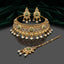 Gold Antique Emerald Green Kundan and Pearl Choker Bridal Set flat lay on dark grey mirror surface with emerald green velvet backdrop showing 3-piece set with wide kundan choker necklace featuring alternating emerald green 4-petal marquise kundan medallions on white enamel base with antique gold filigree fringe and triple pearl drops with matching chandelier earrings and maang tikka with mirror reflection