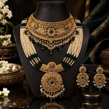 Gold Antique Emerald and Pearl Double Layer Grand Bridal Rani Haar Set displayed on neck stand in Mughal dark backdrop editorial with jasmine flowers showing 3-piece set with wide antique gold filigree choker and long multi-strand seed pearl and emerald bead rani haar with grand oval shield pendant and matching large oval chandelier earrings
