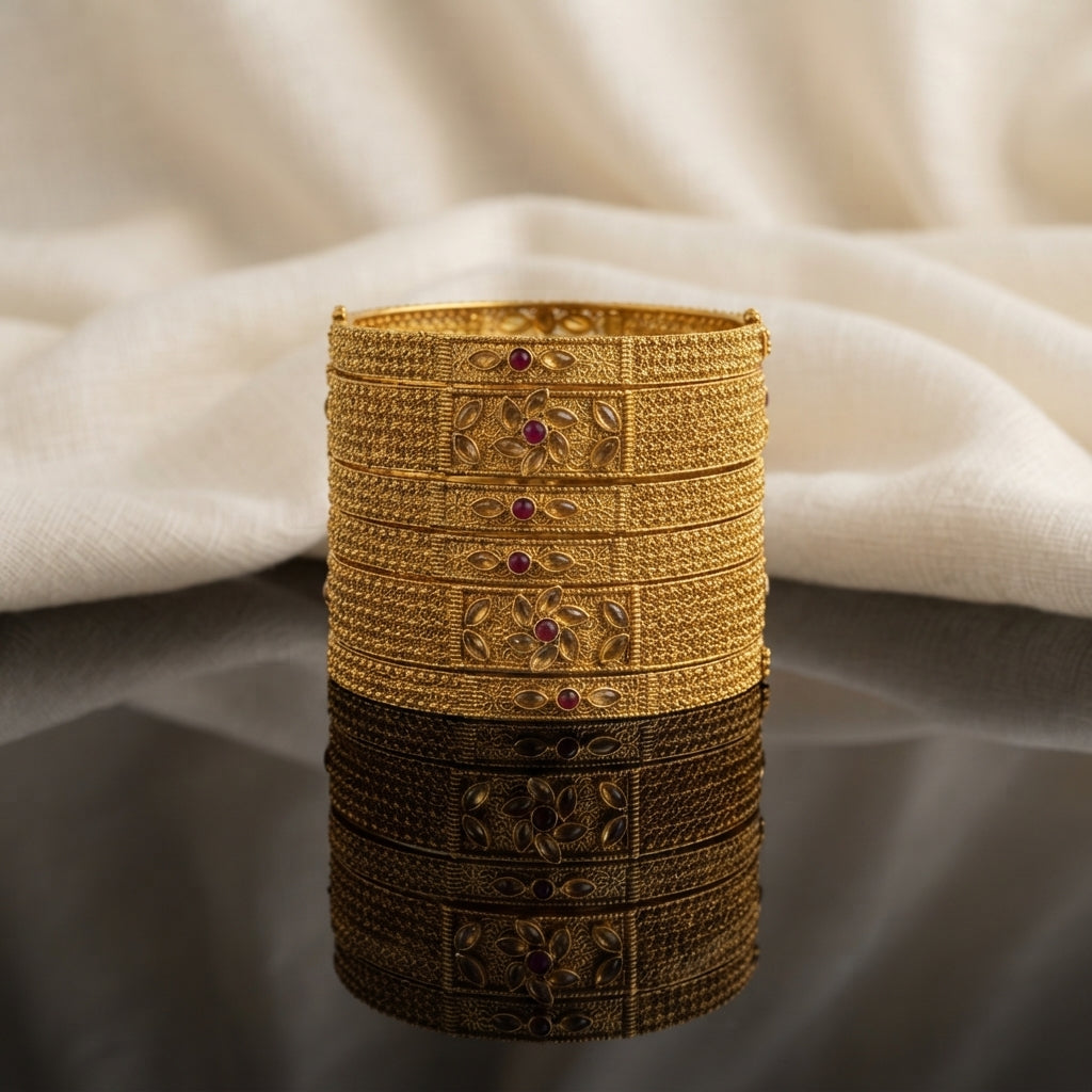 Gold Antique Marquise Polki Ruby Wide Granulation Bangles Set of 4 in 22K antique gold-tone plating on dark grey mirror surface with ivory cream fabric backdrop showing four wide rigid bangles stacked together with full-coverage dense gold granulation seed bead texture and rectangular raised gold frame centre panel featuring 3D marquise polki leaf flower motif with ruby red round cabochon centre and mirror reflection below
