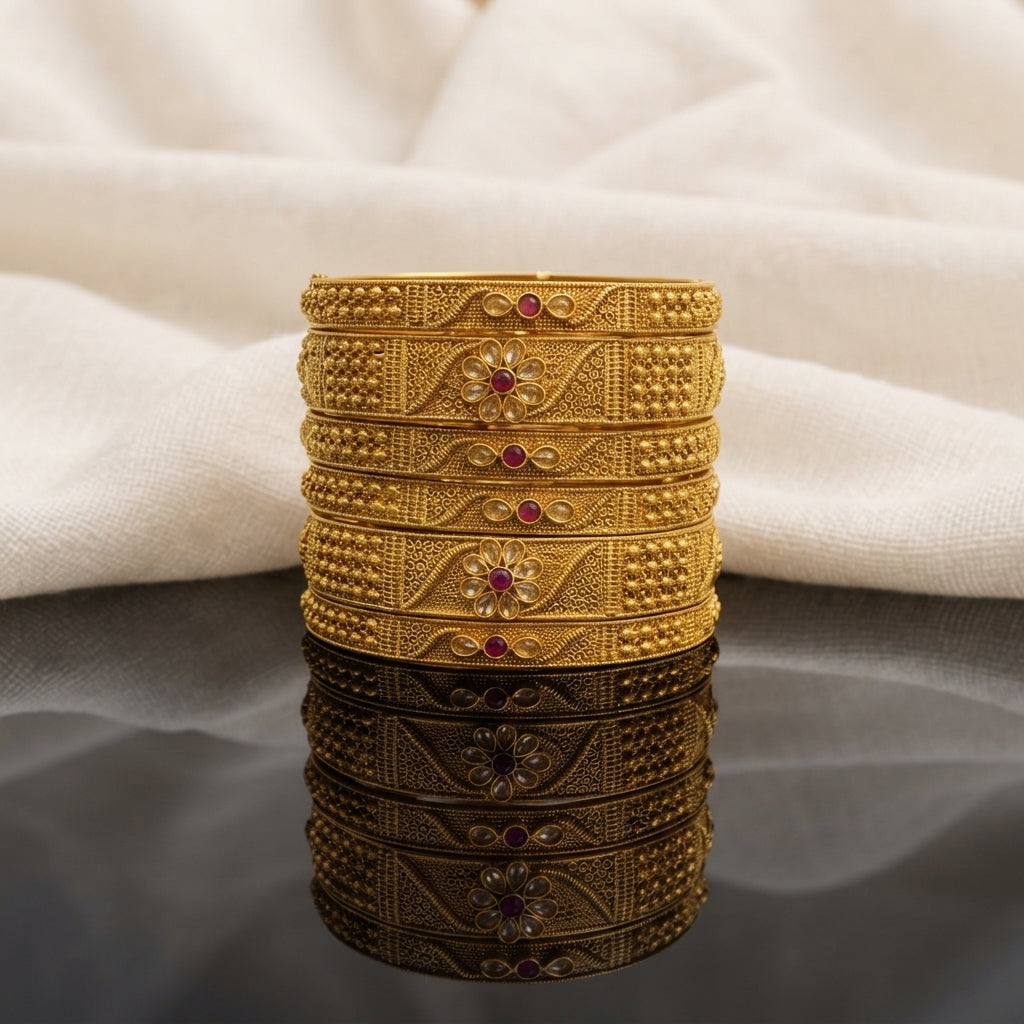 Gold Antique Polki Leaf Vine Floral Ruby Wide Bangles Set of 6 in 22K antique gold-tone plating on dark grey mirror surface with ivory cream fabric backdrop showing six wide rigid bangles stacked together with 3-section band featuring dense gold seed bead granulation panels on sides and diagonal twisted vine filigree with oval polki leaf stones and 3D daisy flower with ruby red cabochon centre with mirror reflection below