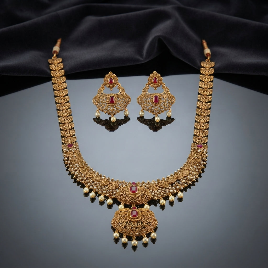 Gold Antique Ruby CZ Filigree Leaf Chain Necklace and Chandbali Earrings Set flat lay on burgundy wine velvet backdrop showing 2-piece set with long graduated filigree leaf-link chain necklace with scattered ruby CZ accents and double-tiered Mughal pendant with pearl fringe drops and matching Chandbali earrings
