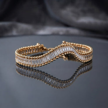 Gold Baguette CZ Channel-Set Double Ball-Edge Wide Tennis Cuff Bracelet flat lay on dark grey mirror surface with dark silk backdrop showing full baguette CZ channel-set center row with double gold ball bead border edges on wide rigid cuff bracelet with mirror reflection below