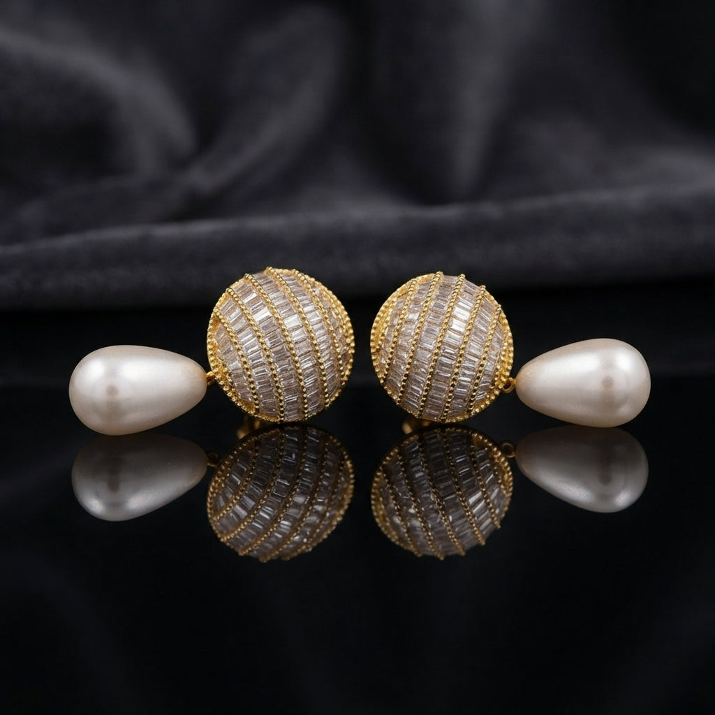 Gold-Tone Baguette CZ Globe Sphere Stud & Pearl Teardrop Drop Earrings on black mirror surface with dark grey silk fabric backdrop