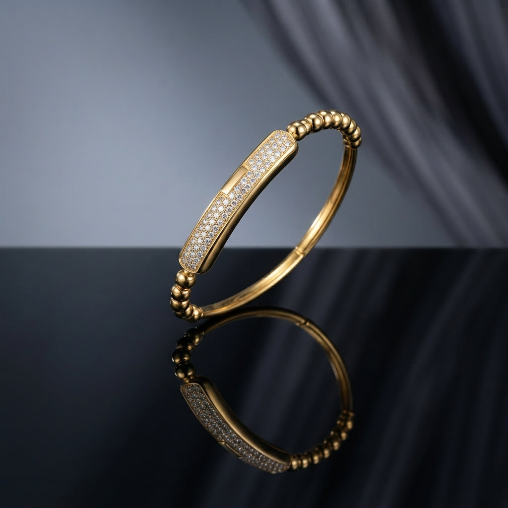 Gold Ball Bead Band Pave CZ Bar Station Rigid Bangle on dark grey mirror surface with grey silk fabric backdrop showing 18K gold-tone rigid bangle with continuous round gold ball bead band and elongated rectangular micro-pave white CZ bar station with geometric gold end caps and hinge clasp with mirror reflection below