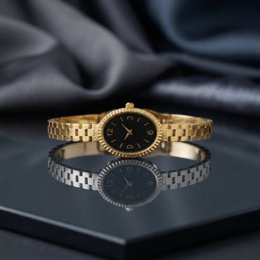 Gold Bangle Bracelet Watch with black dial on dark mirror surface with grey silk backdrop showing 18K gold-tone slim president-style 3-link bracelet with small oval case fluted bezel and black Arabic numeral dial with gold-tone hands with mirror reflection below