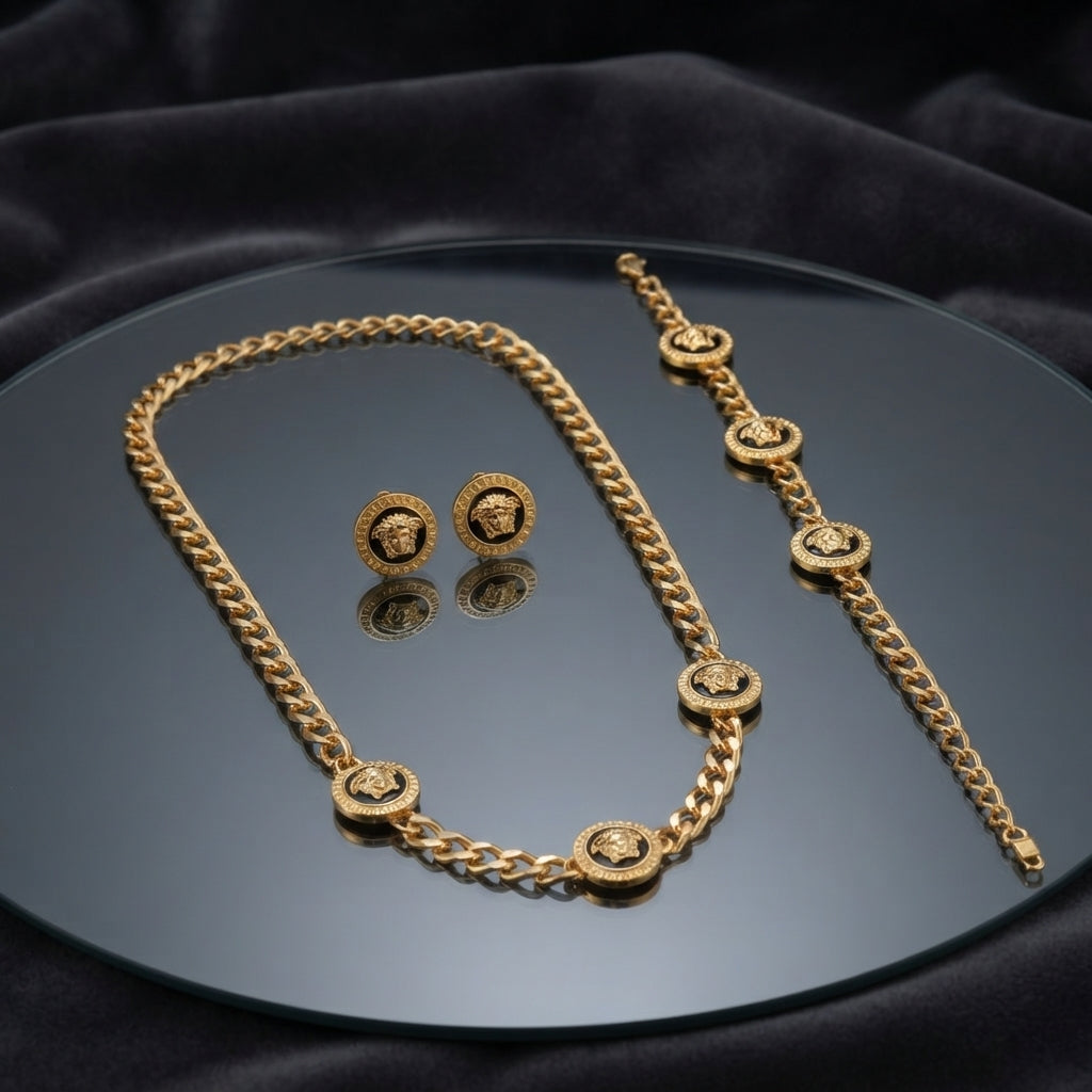 Gold Black Enamel Medusa Head Cuban Chain Necklace Bracelet Earrings Set — 3-piece matching set of heavy 22K gold-tone Cuban curb chain necklace with 5 black enamel Medusa head disc charms, matching bracelet with 5 Medusa disc charms, and black enamel Medusa disc stud earrings, luxury flat-lay on round mirror tray with dark charcoal silk backdrop