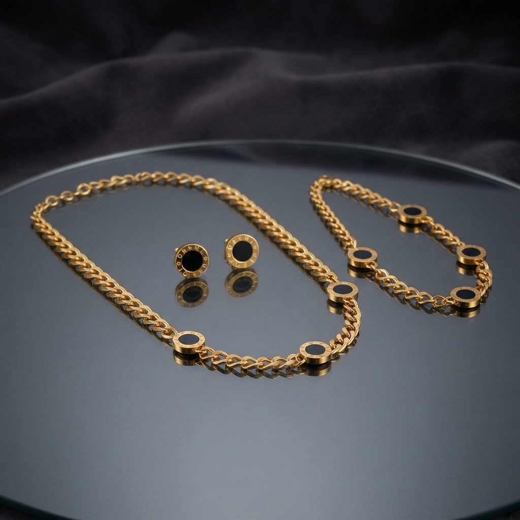 Gold Black Enamel Roman Disc Cuban Chain Necklace Bracelet Earrings Set — 3-piece matching set of heavy 22K gold-tone Cuban curb chain necklace with 5 black enamel Roman disc charms, matching bracelet with 4 disc charms, and round black enamel Roman disc stud earrings, luxury flat-lay on round mirror tray with dark charcoal silk backdrop