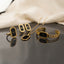 Gold Black Enamel Roman Numeral Clock Face 4-Piece Jewelry Set flat lay on dark grey mirror surface with cream silk backdrop showing full set of micro-pave CZ ring open frame stud earrings pendant necklace and president-link cuff bracelet all with black enamel Roman numeral clock face design with mirror reflections below