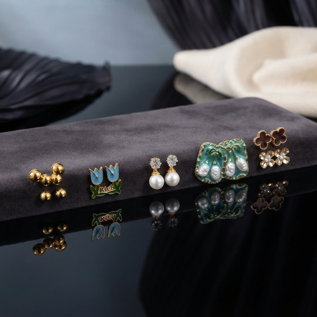 Gold Blue Tulip Floral Enamel Pearl CZ 4-Pair Stud Earring Set flat lay on grey velvet tray with dark blue and cream fabric backdrop showing gold double ball studs blue sky tulip enamel studs with green leaf white CZ pearl drop studs and large teal green enamel square stud with baroque faux pearl drops green leaf brown clover and CZ snowflake cluster with mirror reflections below