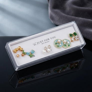 Gold Blue Tulip Mint Floral Pearl Green Clover 4-Pair Stud Earring Set displayed in open clear Just For You acrylic display gift box on black mirror surface with grey velvet backdrop showing all five pairs on white velvet insert with mirror reflection below
