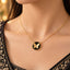 Gold Butterfly Black Onyx Disc Pendant Necklace close-up worn by model in black gold-embroidered formal outfit with gold bokeh backdrop