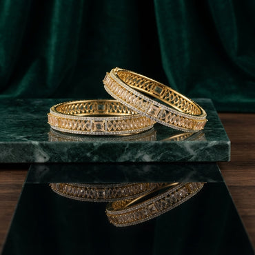 Gold Champagne Baguette CZ Herringbone & White CZ Pavé Wide Bangle Set of 2 stacked on green marble tray with dark green velvet drape backdrop