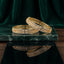 Gold Champagne Baguette CZ Herringbone & White CZ Pavé Wide Bangle Set of 2 stacked on green marble tray with dark green velvet drape backdrop