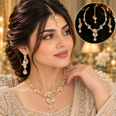 Gold Champagne CZ Floral Vine Necklace Maang Tikka and Linear Drop Earrings Bridal Set — 22K gold-tone 3-piece bridal set with open floral vine necklace with 4-petal CZ flower clusters infinity scroll connectors and champagne pear CZ V-drop matching maang tikka with champagne pear CZ halo drop and 3-tier infinity scroll floral drop earrings displayed on dark mirror surface with black satin backdrop