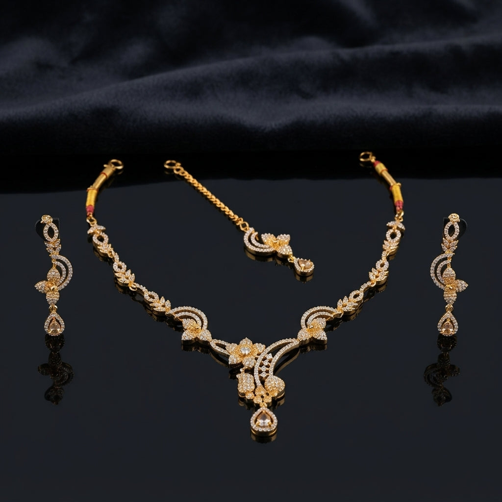 Gold Champagne CZ Floral Vine Necklace Maang Tikka and Linear Drop Earrings Bridal Set — 22K gold-tone 3-piece bridal set with open floral vine necklace with 4-petal CZ flower clusters infinity scroll connectors and champagne pear CZ V-drop matching maang tikka with champagne pear CZ halo drop and 3-tier infinity scroll floral drop earrings displayed on dark mirror surface with black satin backdrop