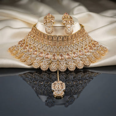 Gold Champagne CZ Grand Pear Lattice Baguette Choker Earrings and Maang Tikka Bridal Set on ivory satin display stand with dark mirror surface showing 22K gold-tone wide choker with champagne CZ cushion baguette top band pear lattice arches fan filigree fringe matching drop earrings and maang tikka