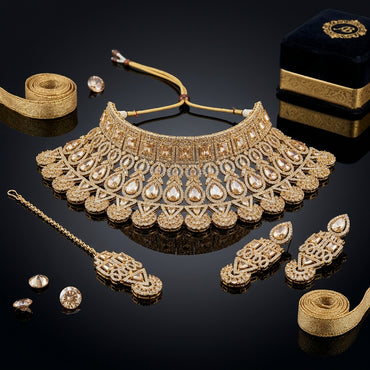 Gold-Tone Champagne CZ Polki Pear & Square Kundan Wide Tiered Scalloped Bib Choker Necklace Drop Earrings & Maang Tikka 3-Piece Bridal Set on black mirror surface with loose champagne CZ stones, gold ribbon and navy blue velvet jewelry box backdrop