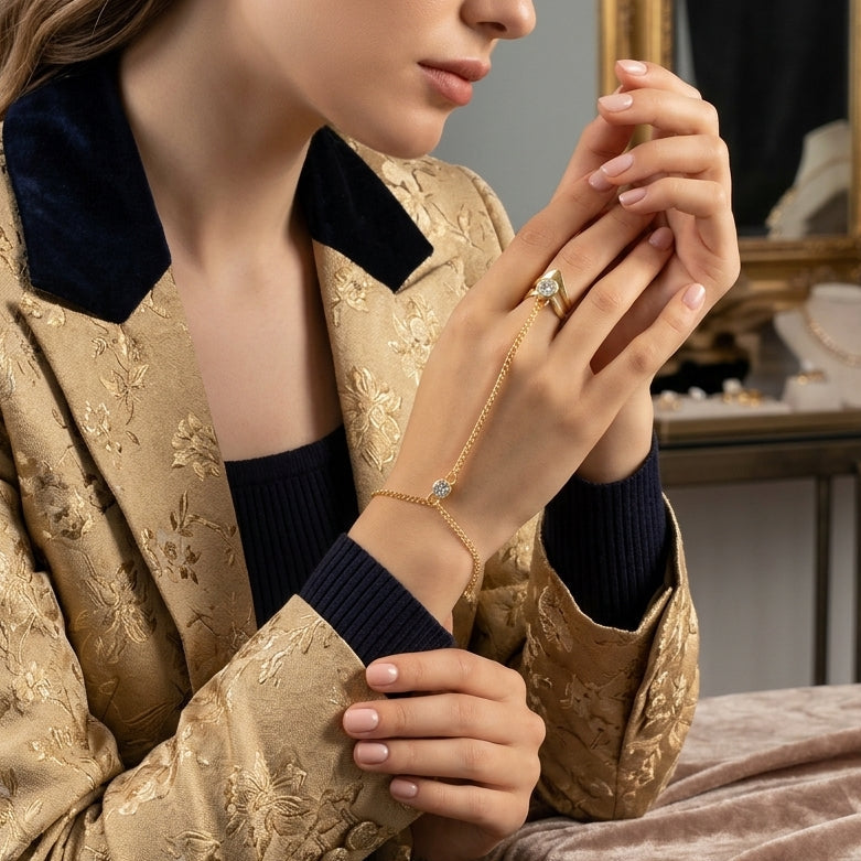 Gold CZ Bezel Double Chevron Arrow Ring Slave Hand Chain Bracelet worn by editorial model in gold brocade jacket with navy collar seated at vanity with gilded mirror backdrop