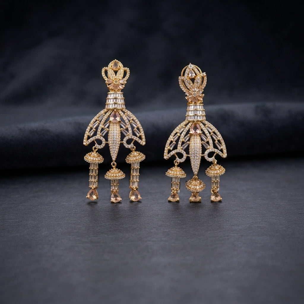 Gold CZ Champagne Baguette Crown and Chandelier Fan Jhumka Drop Earrings on dark charcoal slate surface with dark fabric backdrop showing 22K warm gold-tone grand chandelier jhumka pair with lotus crown baguette column fan chandelier body tiered jhumka bells and morganite pear drops