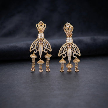Gold CZ Champagne Baguette Crown and Chandelier Fan Jhumka Drop Earrings on dark charcoal slate surface with dark fabric backdrop showing 22K warm gold-tone grand chandelier jhumka pair with lotus crown baguette column fan chandelier body tiered jhumka bells and morganite pear drops