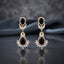 Gold CZ Double Teardrop Marquise Fan Chandelier Earrings in Ruby Red pair on black mirror surface with dark backdrop showing 18K gold-tone small ruby red pear CZ stud with white CZ pave halo infinity connector and large ruby red pear CZ drop with white CZ pave halo and marquise CZ fan crown with mirror reflection below