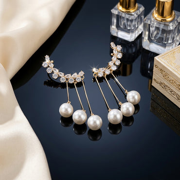 Gold-Tone CZ Ear Crawler Cuff & Triple Pearl Drop Chain Tassel Earrings pair on black reflective surface with ivory silk fabric and gold filigree jewelry box backdrop