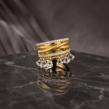 Gold CZ Eternity Twist Band Teardrop Charm 4-Piece Stackable Ring Set side angle view on black marble surface with grey silk backdrop showing layered stack detail of micro-pave CZ eternity bands matte brushed twist band and teardrop CZ briolette charm drops with mirror reflection below