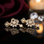 Gold-Tone CZ Pavé Fan & Marquise Leaf Chandelier Drop Earrings product shot on black reflective surface with rose and candle backdrop