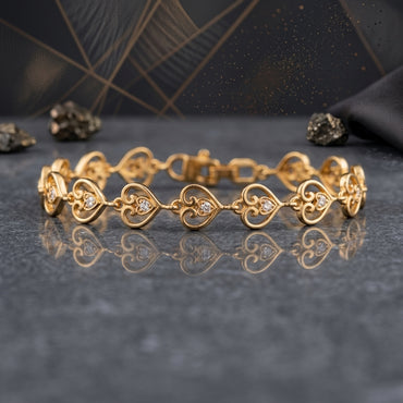 22K Gold-Tone CZ Filigree Heart Link Chain Bracelet on grey stone surface with pyrite mineral crystals and dark charcoal geometric backdrop