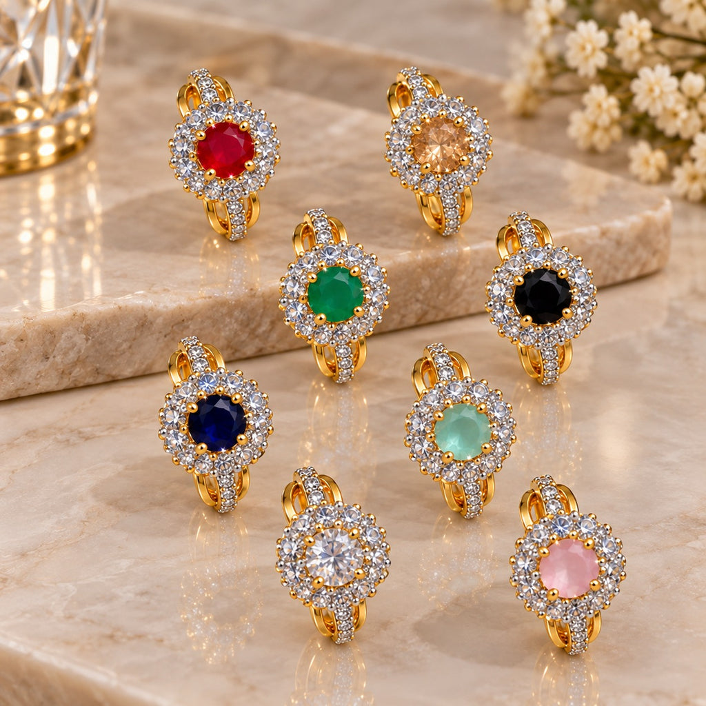 Gold CZ Halo Cocktail Ring with oval coloured CZ centre stone in double white CZ halo cluster and triple split-shank pave band shown in all 9 color variants Ruby Red Champagne Emerald Green Jet Black Navy Blue Mint Green Crystal Clear Baby Pink and Teal arranged on warm marble surface with white floral backdrop in 18K gold-tone plated finish