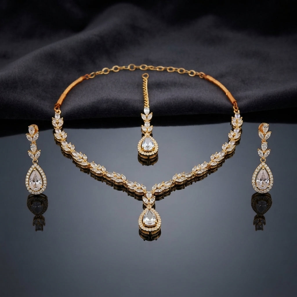 Gold CZ Marquise Leaf Vine Necklace Maang Tikka and Pear Halo Drop Earrings Bridal Set — 18-22K gold-tone 3-piece bridal set with continuous marquise CZ leaf vine necklace with large pear CZ micro-pavé halo V-drop pendant matching maang tikka with pear CZ halo drop and 3-tier marquise leaf linear drop earrings with pear CZ halo displayed on dark grey mirror surface with charcoal satin backdrop