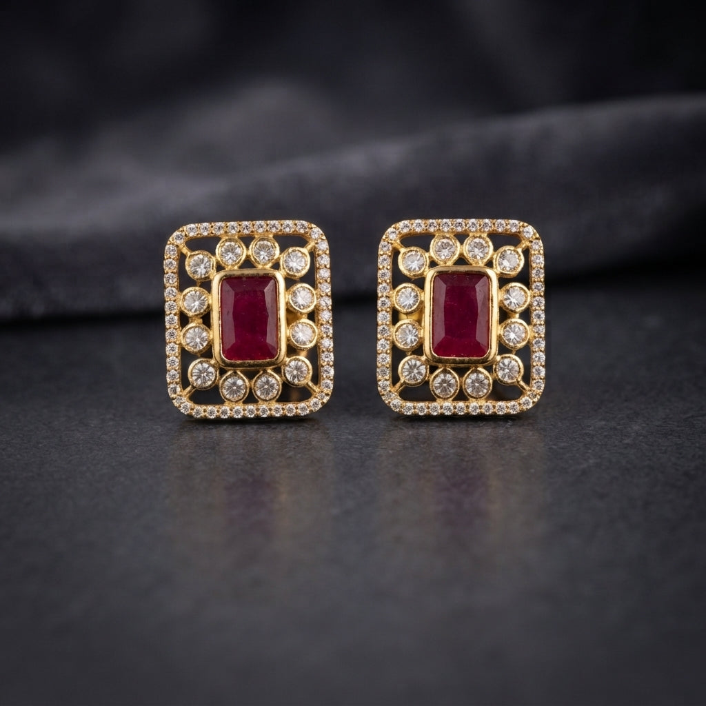 Gold CZ Open Filigree Rectangle Frame and Solitaire Stud Earrings in Ruby Red on dark slate surface with charcoal satin backdrop showing 22K gold-tone open rectangular filigree frame with micro-pave CZ border large round white CZ bezel solitaires and vivid deep ruby red emerald-cut CZ centre stone