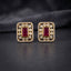 Gold CZ Open Filigree Rectangle Frame and Solitaire Stud Earrings in Ruby Red on dark slate surface with charcoal satin backdrop showing 22K gold-tone open rectangular filigree frame with micro-pave CZ border large round white CZ bezel solitaires and vivid deep ruby red emerald-cut CZ centre stone