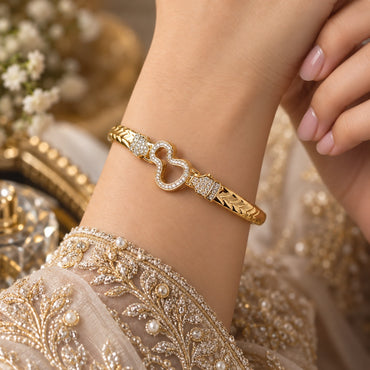 Gold CZ Pave Open Double Heart Bangle Bracelet 4-panel multi-angle collage showing model wear on black embroidered outfit and three product flat lay angles on marble and cream surfaces displaying 18K gold-tone chevron band bangle with open double-heart CZ pave centre and rectangular CZ accent blocks