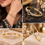 Gold CZ Pave Open Double Heart Bangle Bracelet worn on wrist in bridal editorial close-up showing 18K gold-tone rigid bangle with chevron engraved band open double-heart centre motif fully outlined in white CZ pave flanked by two pave CZ rectangular accent blocks on cream bridal embroidered outfit