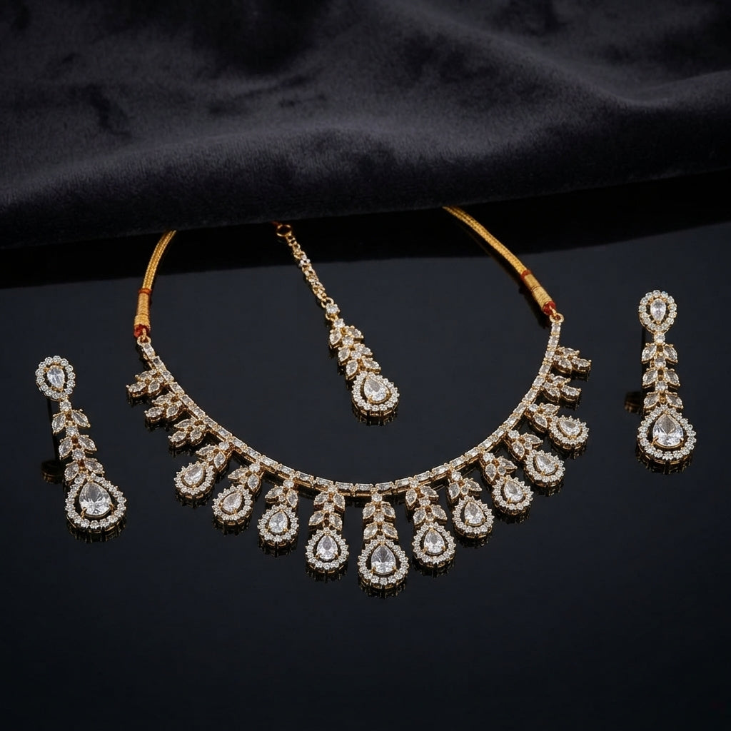 Gold CZ Pear Fringe Necklace Maang Tikka and Linear Drop Earrings Bridal Set — 22K gold-tone 3-piece bridal set with graduating pear CZ halo fringe necklace with marquise leaf clusters and traditional red thread spine matching maang tikka with pear CZ halo drop and 3-tier linear drop earrings displayed on dark black satin surface with mirror reflection